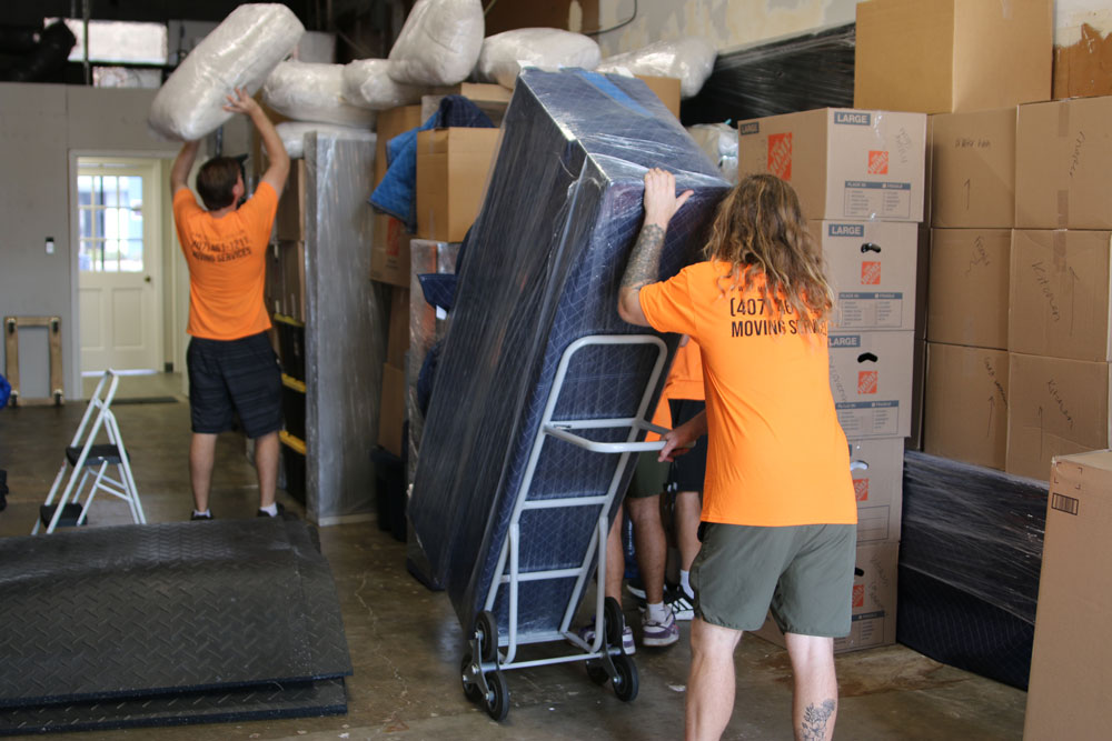 Two MechaMovers movers carrying boxes out of a house
